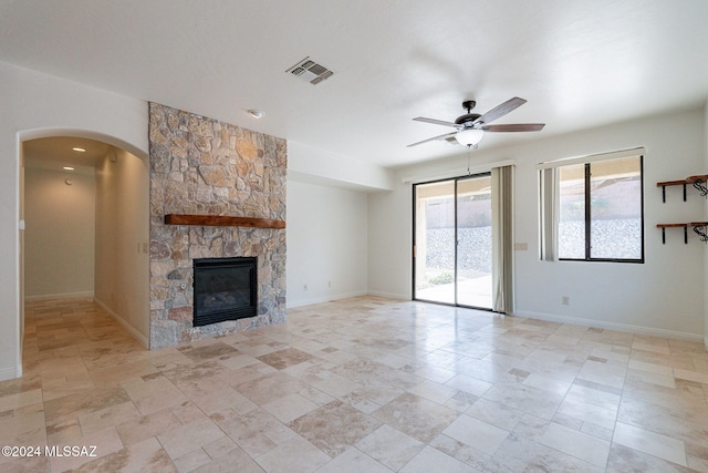 unfurnished living room with ceiling fan, arched walkways, a fireplace, baseboards, and visible vents