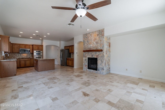 unfurnished living room with a stone fireplace, sink, and ceiling fan