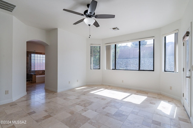 spare room with stone tile floors, a ceiling fan, visible vents, and arched walkways