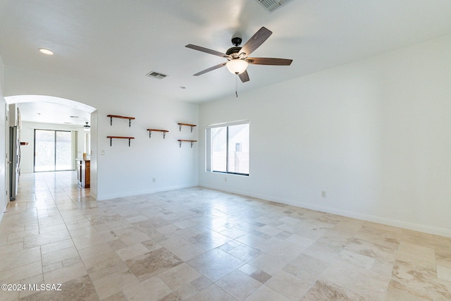 spare room featuring ceiling fan, arched walkways, visible vents, and plenty of natural light
