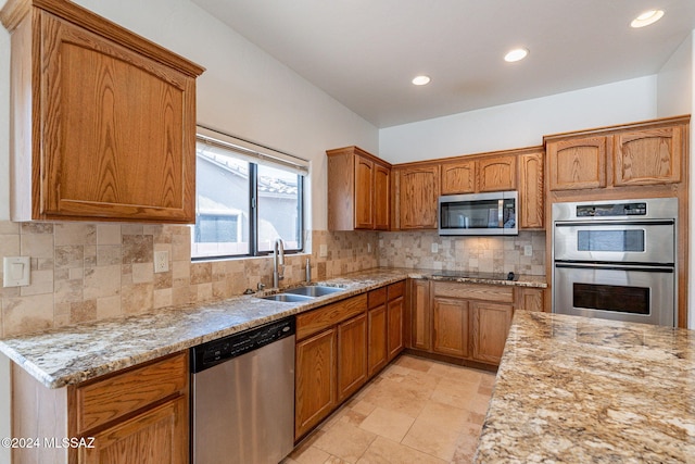 kitchen with brown cabinetry, light stone countertops, appliances with stainless steel finishes, and a sink