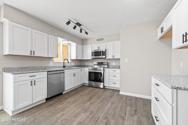 kitchen featuring light stone counters, light hardwood / wood-style floors, sink, white cabinetry, and appliances with stainless steel finishes