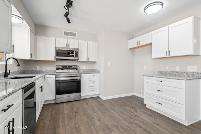 kitchen featuring appliances with stainless steel finishes, dark wood-type flooring, white cabinets, track lighting, and sink