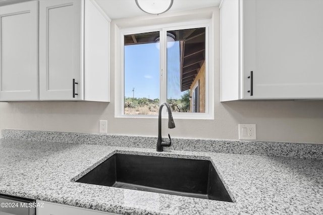 interior details featuring light stone countertops, sink, and white cabinets