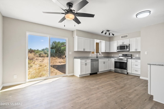 kitchen featuring light wood-type flooring, light stone counters, white cabinetry, stainless steel appliances, and ceiling fan