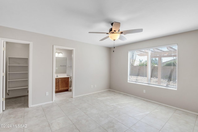 unfurnished bedroom featuring light tile patterned floors, a closet, ceiling fan, a walk in closet, and ensuite bath