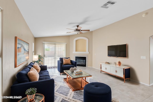 living room featuring vaulted ceiling, ceiling fan, a tile fireplace, and light tile patterned flooring