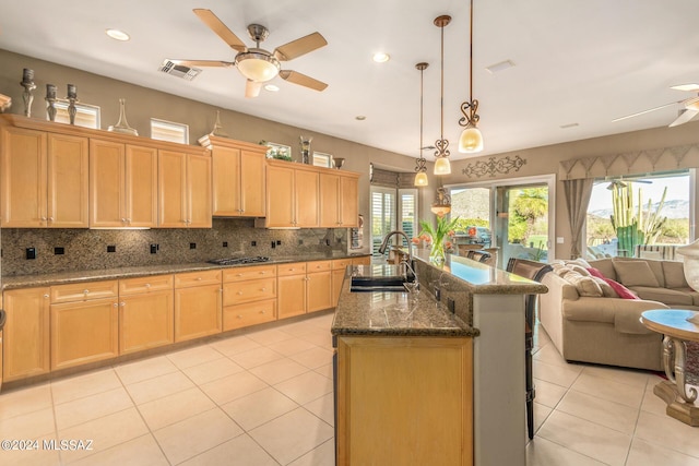 kitchen with sink, dark stone countertops, pendant lighting, ceiling fan, and a kitchen island with sink