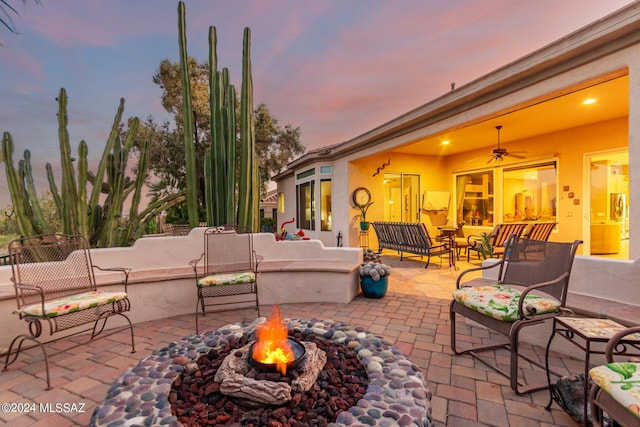 patio terrace at dusk with ceiling fan and an outdoor living space with a fire pit