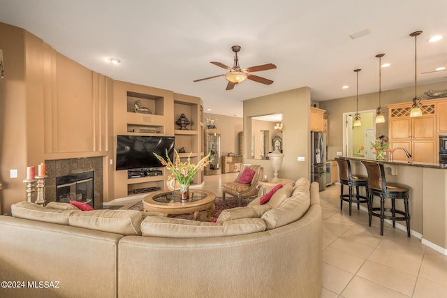 living room with ceiling fan, a premium fireplace, sink, and light tile patterned floors