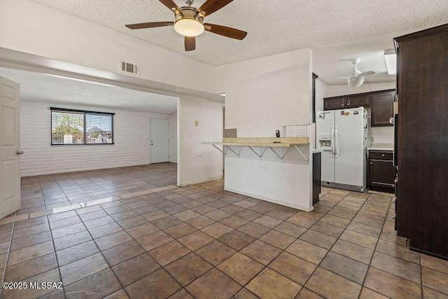 kitchen featuring white refrigerator with ice dispenser, ceiling fan, open floor plan, and a textured ceiling
