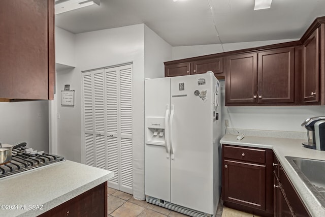 kitchen with light tile patterned floors, stainless steel gas cooktop, dark brown cabinets, white fridge with ice dispenser, and vaulted ceiling