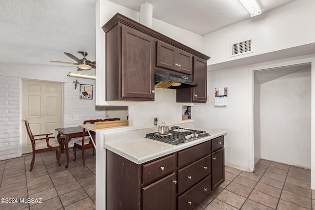 kitchen with a textured ceiling, light tile patterned flooring, stainless steel gas cooktop, dark brown cabinetry, and ceiling fan