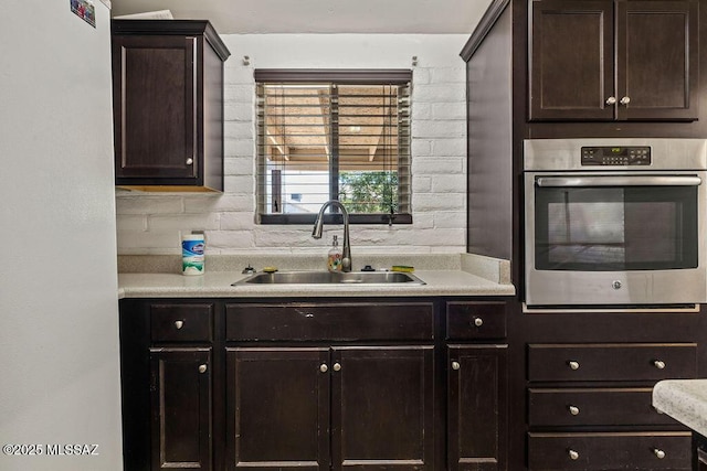 kitchen with dark brown cabinets, light countertops, stainless steel oven, and a sink