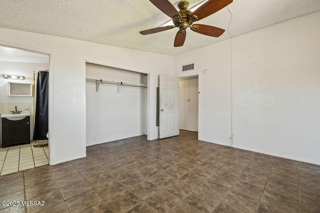 unfurnished bedroom featuring a closet, ceiling fan, ensuite bath, visible vents, and a textured ceiling