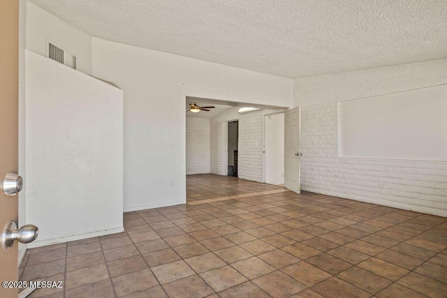 empty room with ceiling fan, a textured ceiling, visible vents, and brick wall