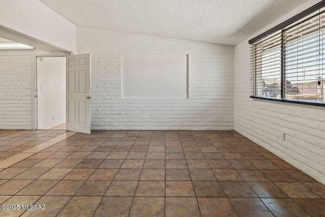 tiled empty room featuring a textured ceiling, lofted ceiling, and brick wall