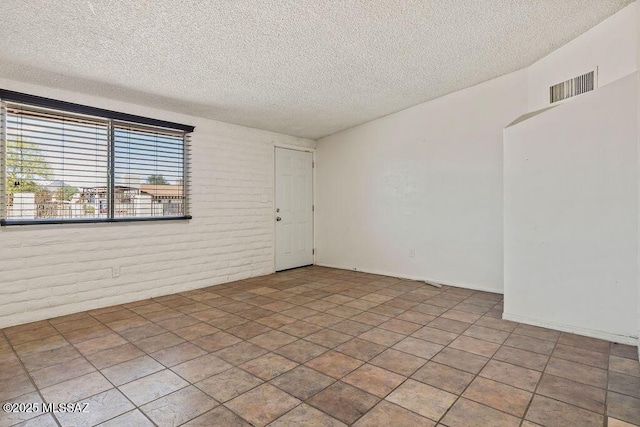 empty room with a textured ceiling, visible vents, and brick wall