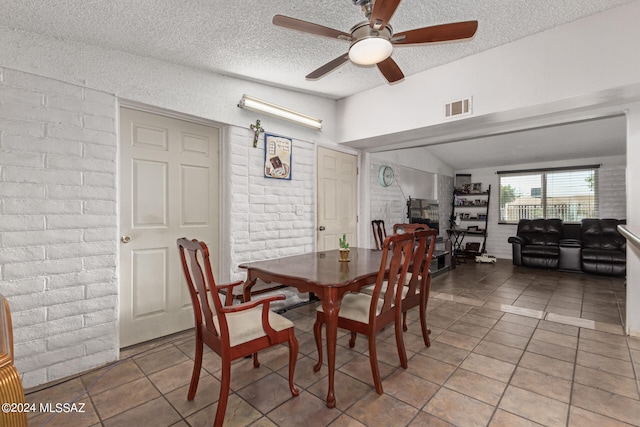 dining area with a textured ceiling, lofted ceiling, light tile patterned floors, ceiling fan, and brick wall