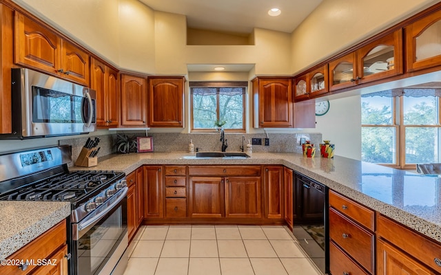 kitchen with light stone countertops, sink, kitchen peninsula, lofted ceiling, and appliances with stainless steel finishes