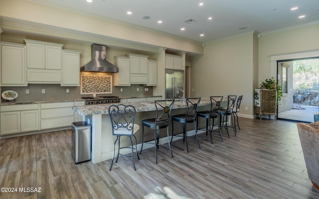 15251 N Dove Canyon Pass, Marana, AZ 85658 - kitchen featuring wall chimney exhaust hood, a kitchen island with sink, light wood-style flooring, ornamental molding, and tasteful backsplash