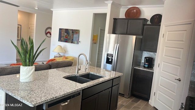 kitchen with light stone counters, ornamental molding, stainless steel appliances, sink, and a center island with sink