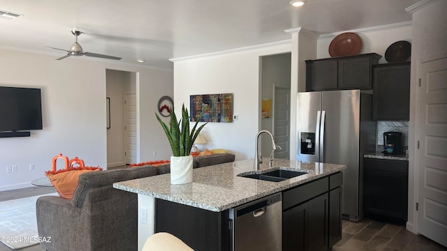 kitchen featuring ceiling fan, sink, stainless steel appliances, light stone counters, and an island with sink