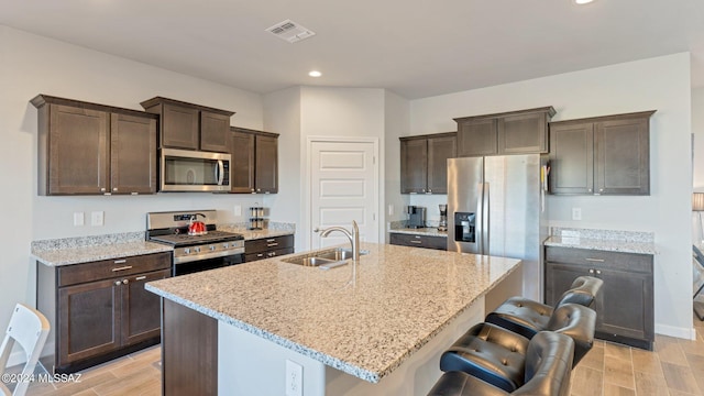 kitchen with appliances with stainless steel finishes, a center island with sink, sink, and light hardwood / wood-style flooring