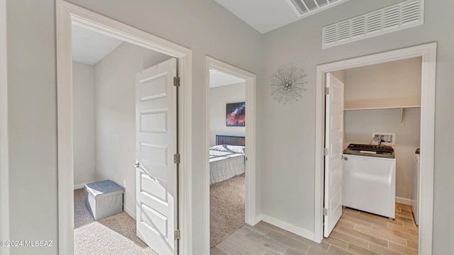 hall with light colored carpet and washer and dryer