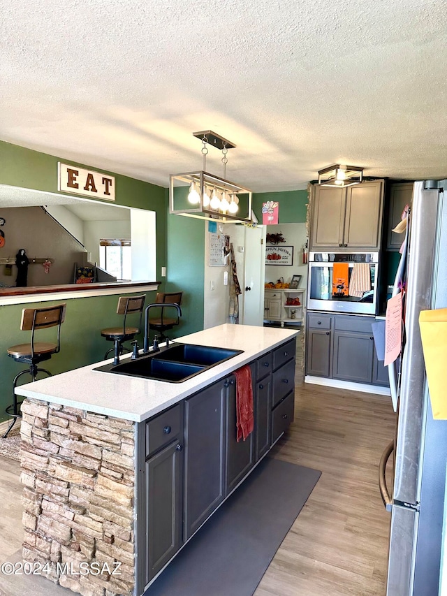 kitchen with pendant lighting, wood-type flooring, appliances with stainless steel finishes, and a kitchen island with sink