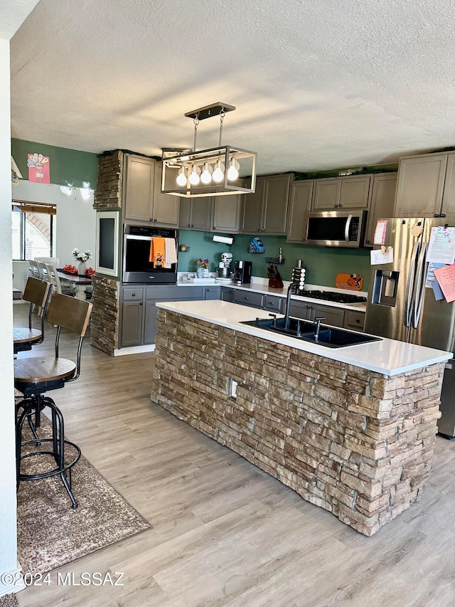 kitchen featuring pendant lighting, light hardwood / wood-style floors, a textured ceiling, stainless steel appliances, and a center island with sink