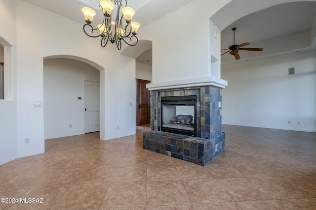 unfurnished living room featuring tile patterned flooring, a towering ceiling, ceiling fan with notable chandelier, and a tiled fireplace