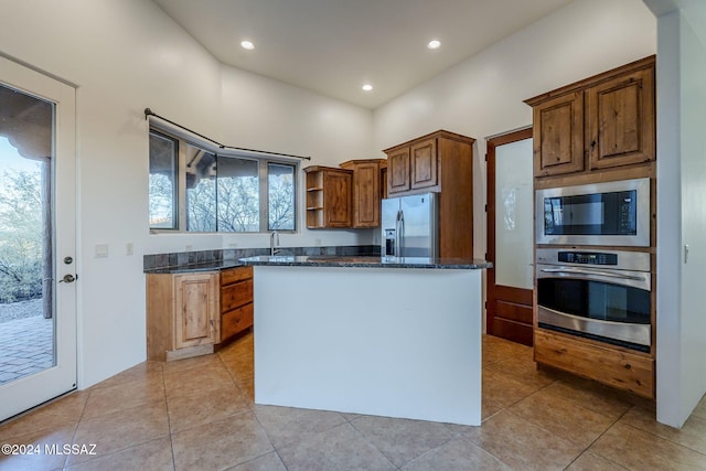 kitchen with a kitchen island, light tile patterned floors, stainless steel appliances, and dark stone counters