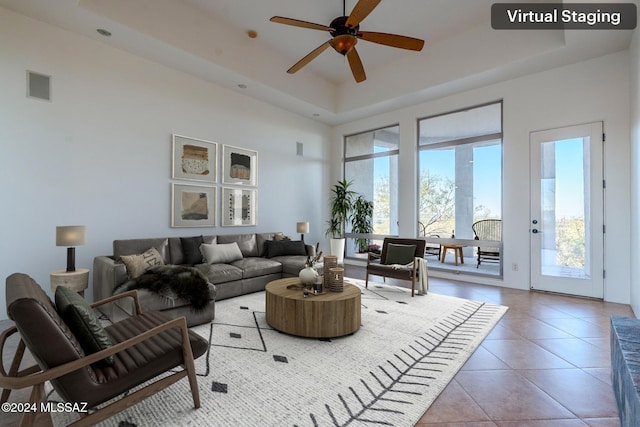 tiled living room with a high ceiling, a tray ceiling, and ceiling fan