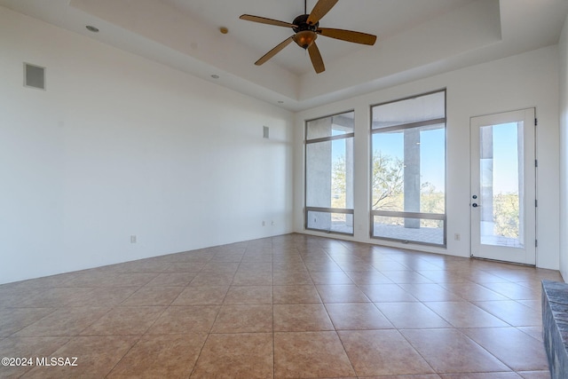 tiled empty room featuring a tray ceiling and ceiling fan