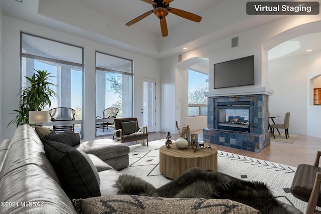 living room with a raised ceiling, a tile fireplace, ceiling fan, and light tile patterned flooring