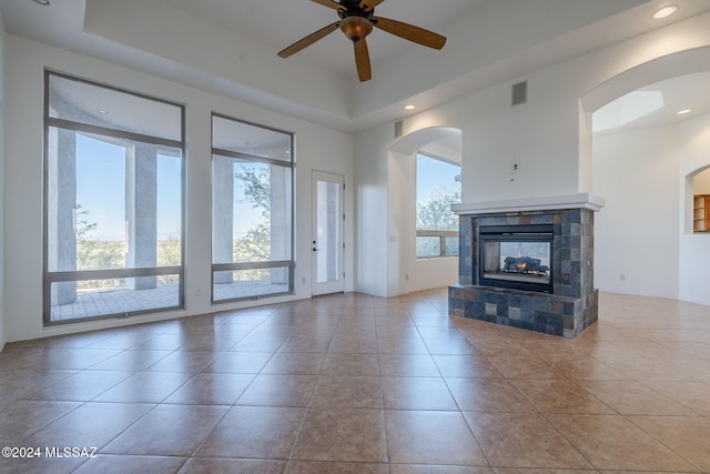 unfurnished living room featuring a tile fireplace, light tile patterned floors, a tray ceiling, and ceiling fan