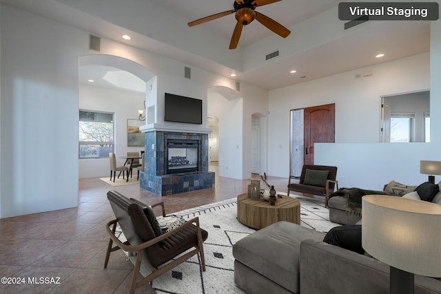 tiled living room with ceiling fan, a towering ceiling, and a fireplace