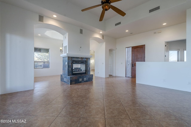 unfurnished living room with a fireplace, light tile patterned floors, ceiling fan, and a high ceiling