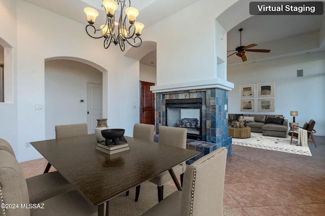 dining space featuring tile patterned floors, ceiling fan with notable chandelier, a high ceiling, and a tiled fireplace