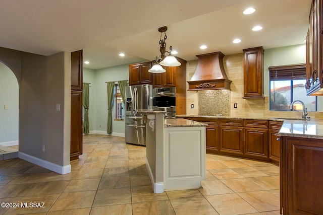 kitchen featuring light stone counters, custom range hood, sink, stainless steel refrigerator with ice dispenser, and a center island