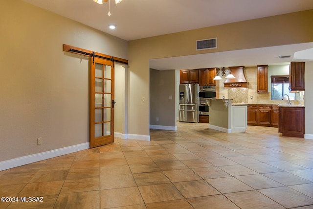 kitchen with a barn door, a kitchen island, backsplash, custom range hood, and stainless steel fridge with ice dispenser