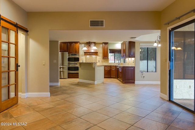 kitchen featuring appliances with stainless steel finishes, a barn door, a kitchen island, hanging light fixtures, and decorative backsplash