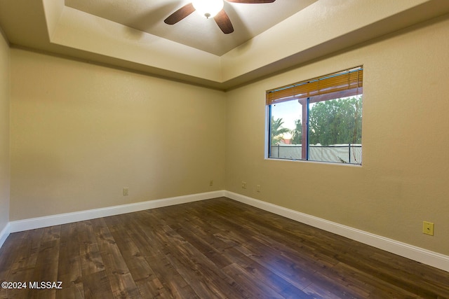 empty room featuring ceiling fan, a tray ceiling, and dark hardwood / wood-style flooring