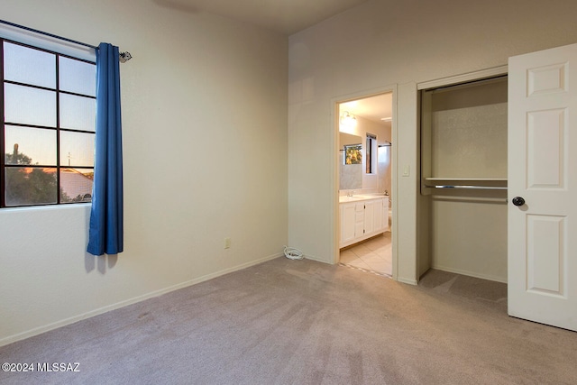 unfurnished bedroom featuring light carpet, ensuite bathroom, and sink