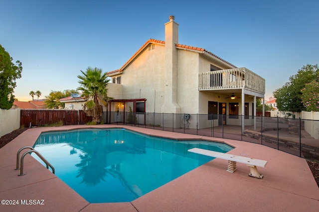 pool at dusk with a patio area and a diving board