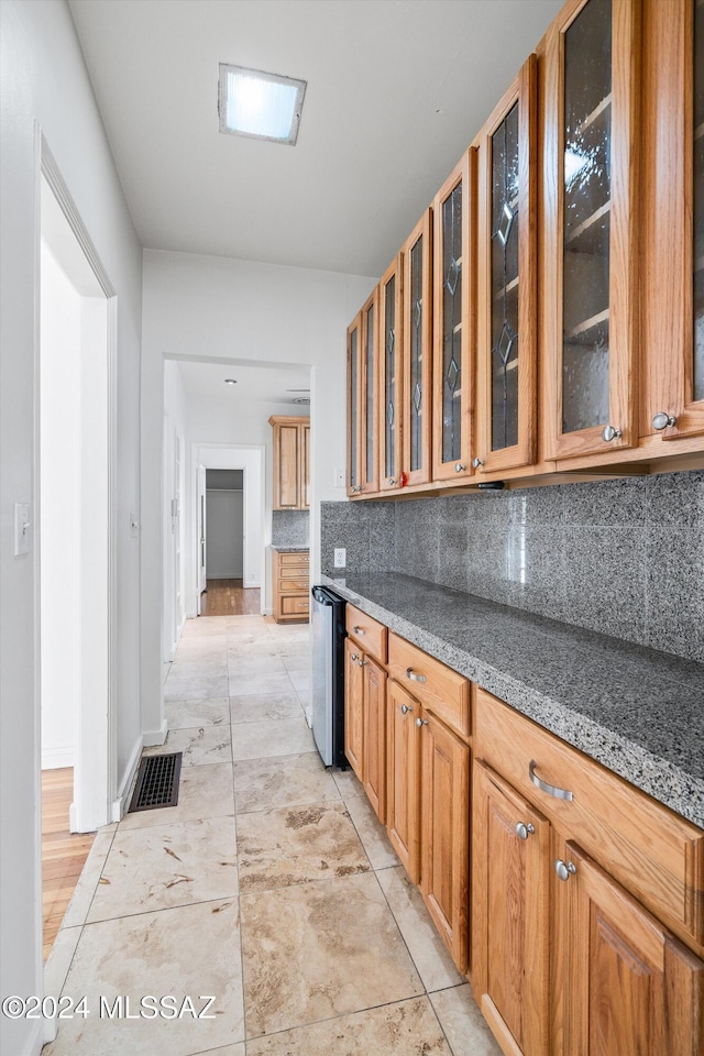 kitchen with tasteful backsplash, dark stone counters, dishwashing machine, and light tile patterned flooring