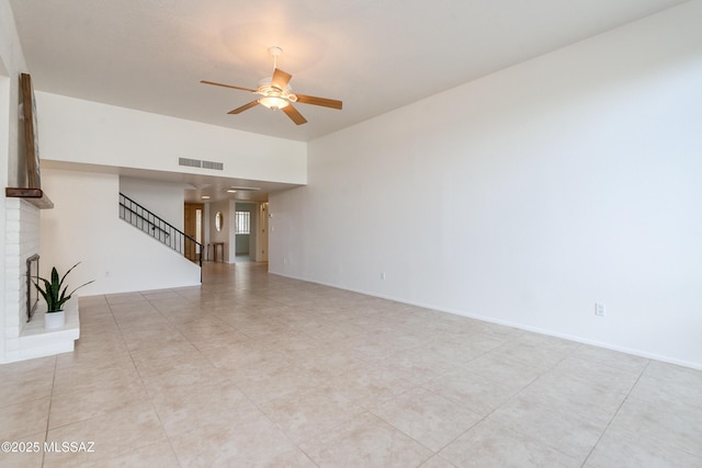 unfurnished living room featuring visible vents, baseboards, ceiling fan, stairs, and a brick fireplace