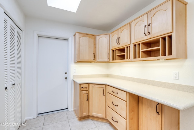 kitchen featuring light countertops, a skylight, light tile patterned floors, and light brown cabinetry