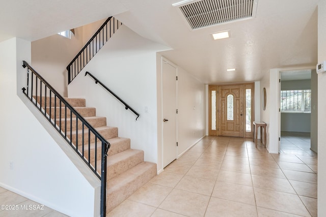 entryway with light tile patterned floors, baseboards, stairs, and visible vents